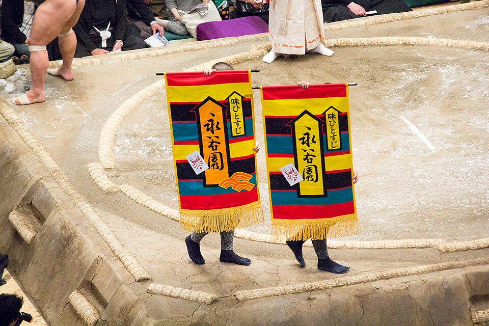 Attendants carrying sponsor banners in a circle around the sumo ring.